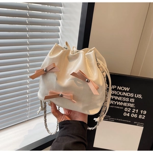 Détail d'un sac seau blanc avec des nœuds en cuir rose et une bandoulière en chaîne