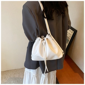 White leather drawstring bucket bag worn by model with minimalist grey blazer and long skirt