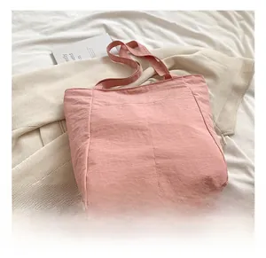 Detail of pink canvas tote bag with textured fabric and long handles on white linen