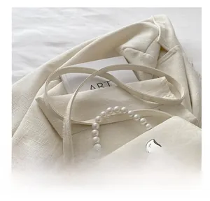 Detail of cream pearl handle handbag with a metal bow clasp on a textured blazer