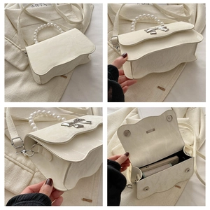 Detail of cream crossbody bag featuring pearl handle, metal bow, and wavy edges