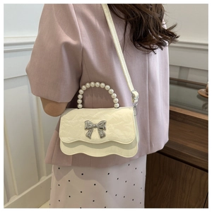 Detail of cream white pleated shoulder bag with pearl handle and silver bow on flap