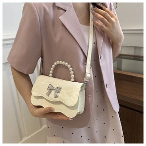 Detail of a beige textured leather crossbody bag with pearl handle and silver bow