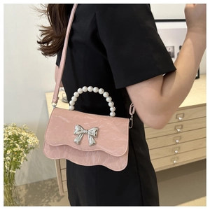 Close-up of pink crossbody bag with pearl handle, silver bow and ruffled flap detail