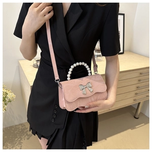 Detail of pink bow handbag with pearl handle and metallic finish on a black dress