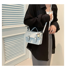 Detail of light blue messenger bag with dual decorative buckles and a cute sheep charm