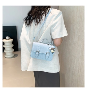 Detailed view of light blue messenger bag with silver buckles and cute girl charm on model