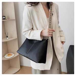 Detail of black pebbled leather shoulder bag with wide geometric woven strap on model