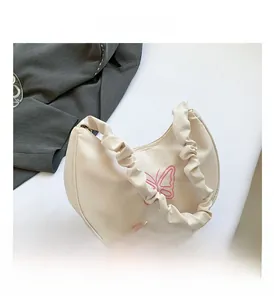 Detail of beige half-moon bag featuring pink butterfly embroidery and a ruched strap