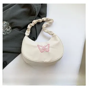 Close-up of pink butterfly embroidery and pleated strap on the beige shoulder bag