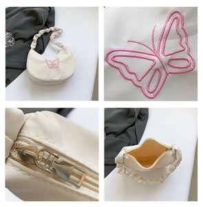 Detail view of butterfly embroidery and pleated strap on white crescent underarm bag