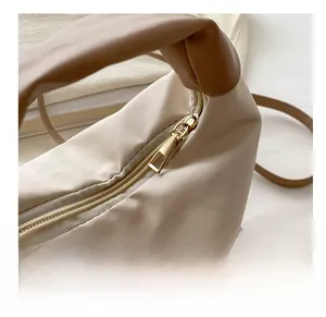 Detail of smooth gold zipper and clean stitching on beige pleated crossbody bag