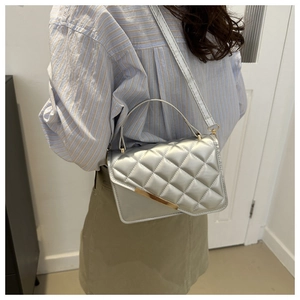 Gros plan sur le sac bandoulière argenté matelassé avec bordure dorée sur tenue rayée