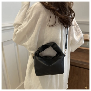 Detailed view of a black pleated handle crossbody bag worn on model's shoulder