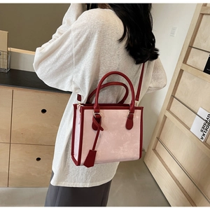 Dettaglio della borsa tote rosa marmorizzata con manici rossi portata a spalla dal modello