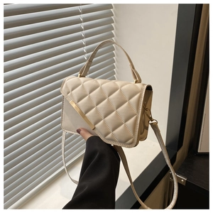 Détail d'un sac à main matelassé blanc crème avec garniture en métal doré tenu par un modèle