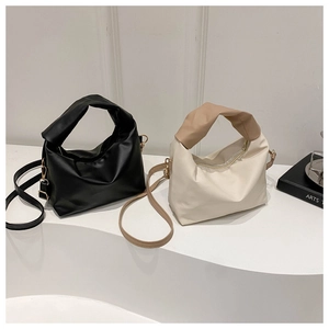 Close-up of pleated small square bags in black and beige with knotted handles and straps
