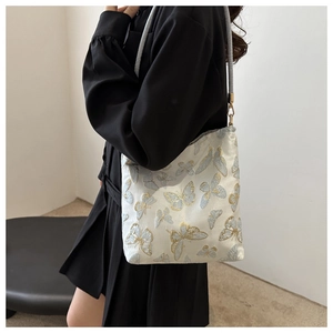 Detailed close-up of intricate butterfly silk embroidery on an elegant cream shoulder bag