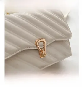 Close-up of white quilted leather handbag with gold irregular metal clasp and chain