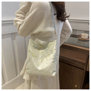 Detailed close-up of silk embroidery with bamboo and bird patterns on a white shoulder bag