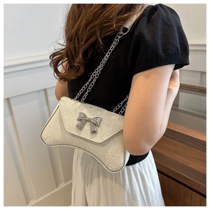Detail of white glitter chain bag with silver bow buckle worn on a model's shoulder