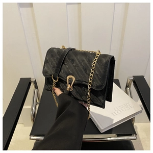 Detail of black quilted shoulder bag featuring gold chain strap and stylish metal clasp