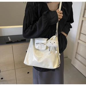 Detailed view of a white glossy leather tote bag featuring a decorative bow and plush charm