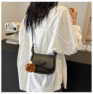 Fashionable black faux leather crossbody bag with a brown plush pompom on a model