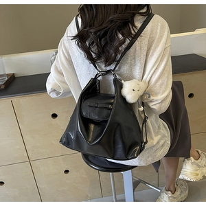 Detail view of black matte PU leather backpack with a white plush cloud charm accessory
