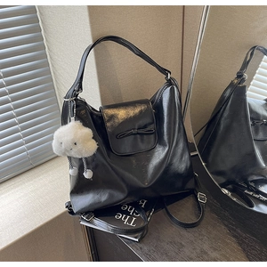 Close-up of black faux leather handbag with bow detail and white plush cloud pendant