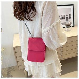 Detail of rose red crossbody phone bag with slim black chain strap shown on a model