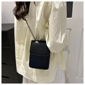 Détail d'un petit sac bandoulière noir minimaliste avec bandoulière en chaîne mate