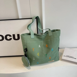 Light green canvas tote bag with colorful letter embroidery and small round charm