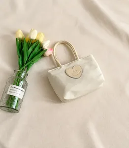 Vista dettagliata della mini borsa crema con toppa a cuore accanto a uno smartphone