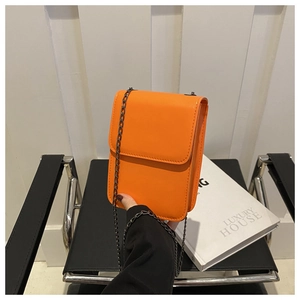 Detail of bright orange mini crossbody bag with black metal chain strap on books