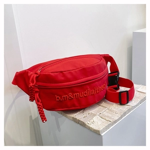 Détail d'un sac banane rouge en nylon avec broderie de lettres et sangle ajustable