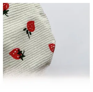 Détail macro du tissu en velours côtelé blanc avec motifs de fraises rouges brodées