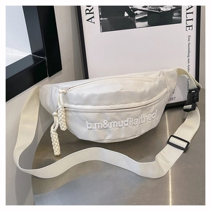 Détail d'un sac banane en toile blanche avec broderie et sangle réglable sur une table
