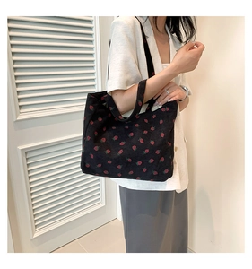 Détail d'un sac cabas en velours côtelé noir à motif fraises porté par un mannequin