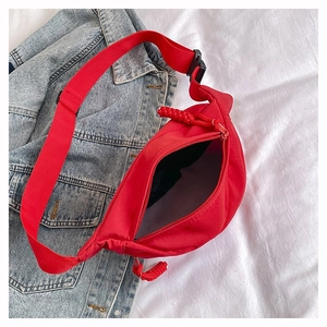 Détail d'un sac banane rouge en nylon avec tirette tissée sur fond de veste en jean