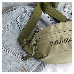 Détail du sac banane en nylon vert armée avec logo noir brodé sur fond de jean bleu