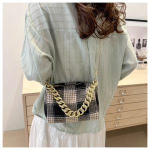 Détail du sac bandoulière à carreaux avec chaîne dorée porté par un mannequin en intérieur