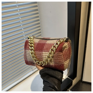Gros plan d'un sac cylindrique en tweed à carreaux rouge et beige avec chaîne dorée
