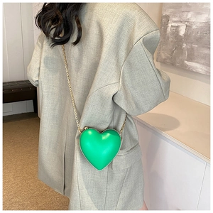 Modèle portant un sac bandoulière vert en forme de cœur avec une fine chaîne dorée