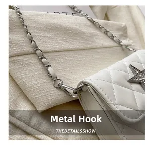 Close-up of silver metal hook and woven chain strap on white quilted crossbody bag