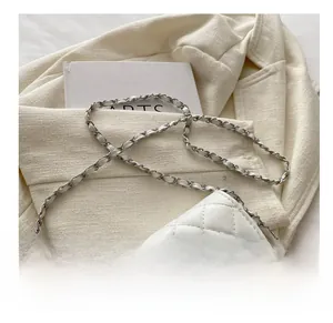 Detail of white quilted crossbody bag featuring a sparkling star buckle and chain strap