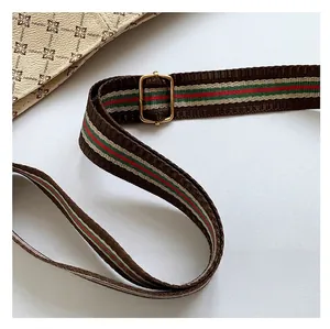 Detail of adjustable woven brown shoulder strap with red and green stripes and gold buckle