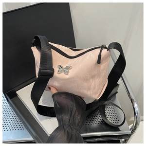 Detail van lichtroze crossbodytas met zilveren vlinder en zwarte schouderriem
