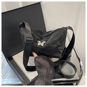 Detail van zwarte crossbodytas met rimpeltextuur en een zilveren metalen vlinderaccent