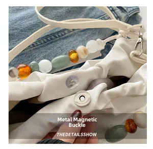 Detail view of a white crossbody bag featuring magnetic metal closure and decorative resin beads